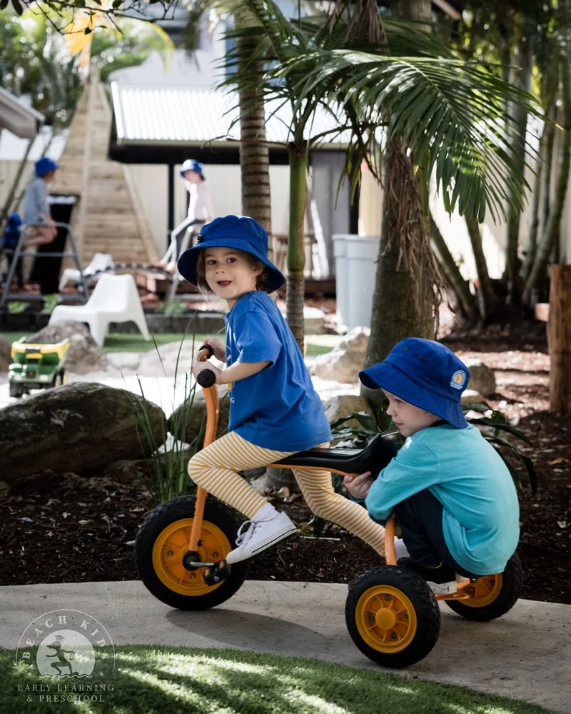 Two children in Beach Kids hats riding a trike together at Cabarita