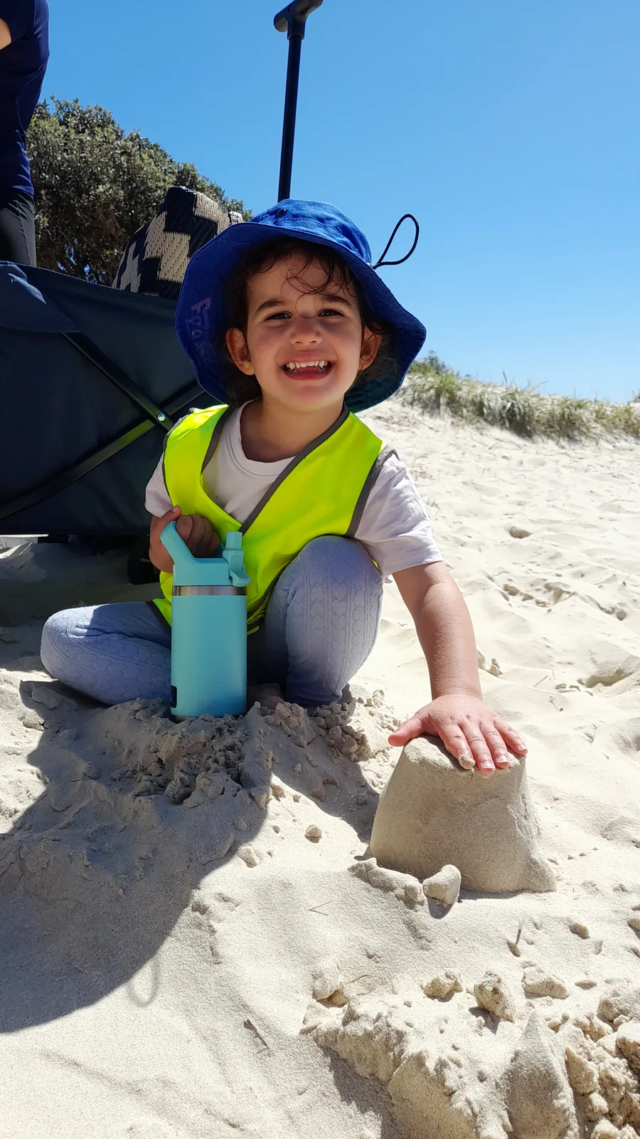 A child in a blue Beach Kids hat building with damp sand