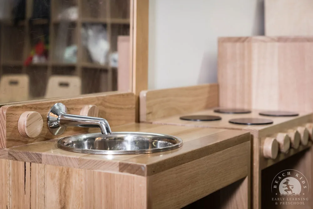 A timber mud kitchen with a stainless sink and tap at Beach Kids Cabarita
