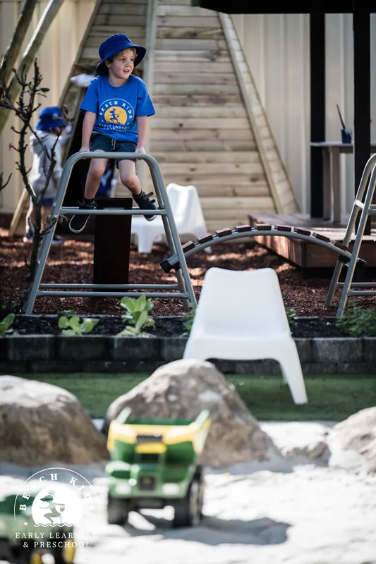 A child climbing the outdoor frame beside the sandpit at Beach Kids