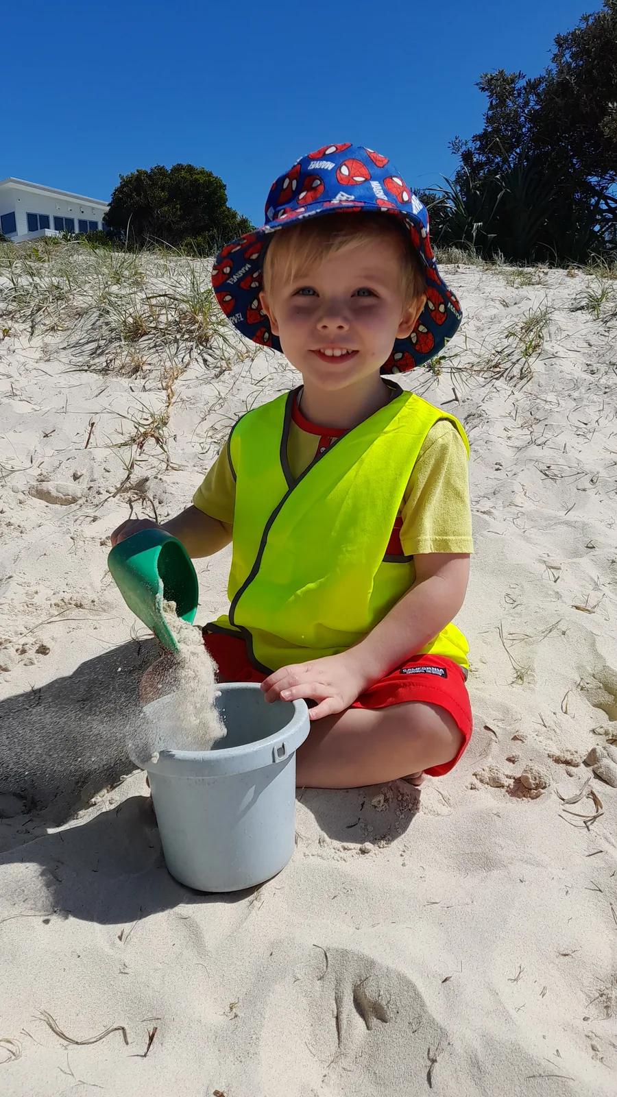 A child in a red Beach Kids hat exploring wet sand