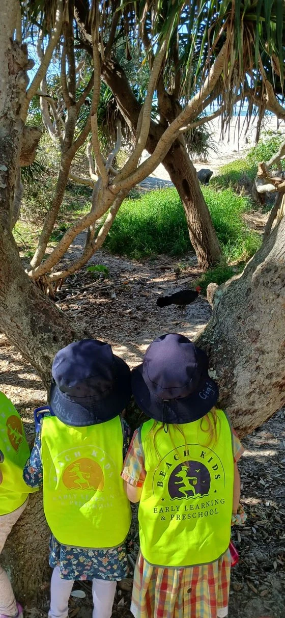 Two children watching a brush turkey under the pandanus trees near the beach