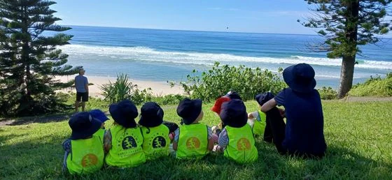 Beach Kids children in hi-vis vests sitting on the grass looking out to the ocean during Beach Kinder